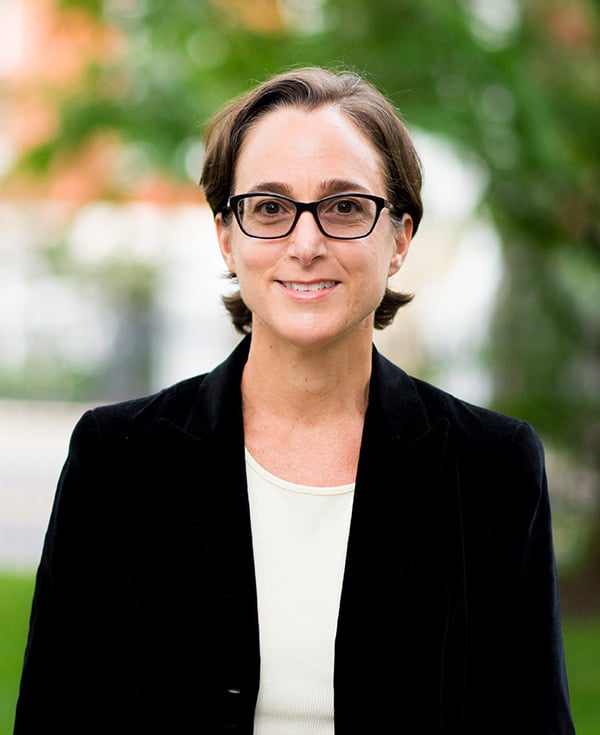 A photo of Maria LaHood. She is a fair skinned woman, with short brown hair. She's wearing a black blazer with a white top and black glasses.