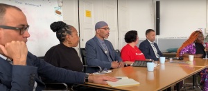 Still photo from the recording. The panel is sitting, from left to right: Robert Saleem Holbrook, Patricia Vickers, Stanley Jamel Bellamy, Kelly Savage-Rodriguez, Anthony Hingle and Nikki Grant. Nikki grant is holding the microphone.
