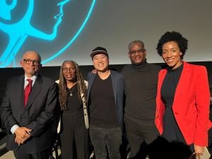 Photo of the panelists after the film screening. They are standing next to each other, smiling with their arms around one another.   Pictured Left to Right, former Center for Constitutional Rights attorneys Randolph M. McLaughlin and Betty Lawrence Lewis, filmmaker John Beder, Executive Director Vincent Warren, and Associate Director of the Southern Regional Office Emily Early.