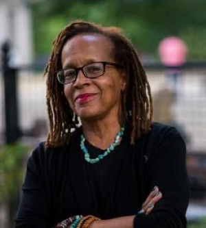 Photo of Theda Jackson-Mau, outgoing Director of Development who is retiring in May 2024. She is facing the camera with a smile on her face, she has her arms crossed. She is wearing black glasses, a black top, a turquoise necklace, and bracelets.