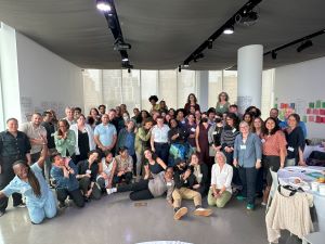 Group photo from our convening. dozens of staff members posing for a silly photo. Many people are smiling at the camera or at each other.