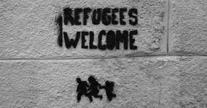 'Refugees welcome' graffiti on a cinder block wall.