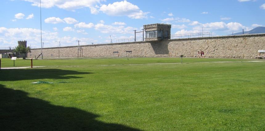A prison yard with grass, stone walls, and a tower.