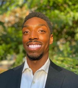 Headshot of Remy Burtonds in gray blazer with white buttondown shirt