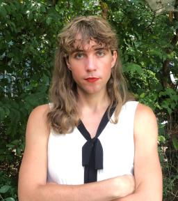 Headshot of Zee Scout with arms crossed in sleeveless white blouse with black bow