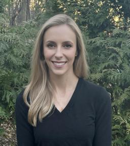 Headshot of Elizabeth in a longsleeved black v-neck short in front of greenery