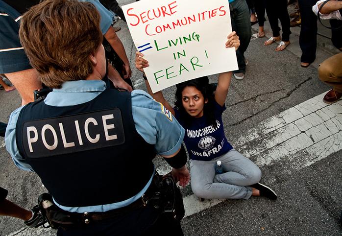 A protester holds up a sign while sitting on the ground, as a police offer stands over.
