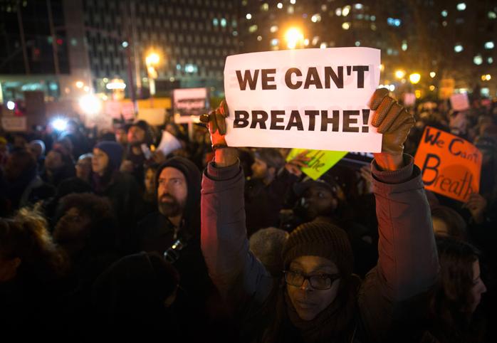 Woman at a protest holds a sign that says "We Can't Breathe!"