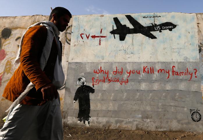 Man walks past wall with graffiti of a U.S. drone and a small boy writing "why did you kill my family?"