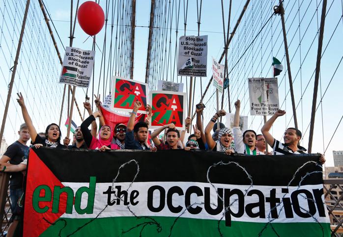 Protestors march across the Brooklyn Bridge holding a banner that reads "End the Occupation"