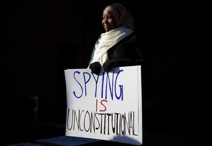 A woman holds a sign that reads "spying is unconstitutional"
