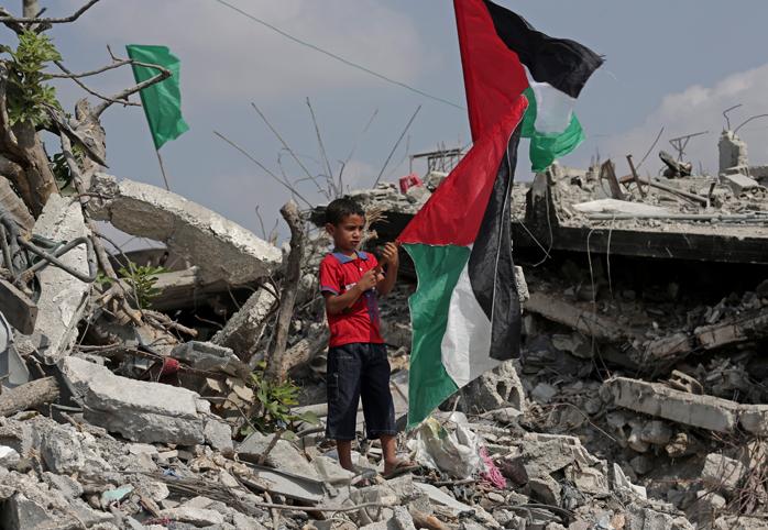Young boy stands in rubble holding Palestinian flag