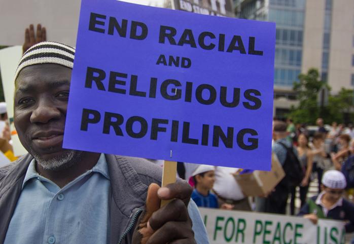 Protestor holds a sign that says "End Racial and Religious Profiling"