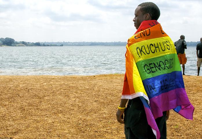 Man wearing a rainbow flag that reads "End LGBTI (Kuchu's) Genocide in Uganda"