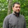 Headshot of Brad in gray button-down shirt in from of green foliage